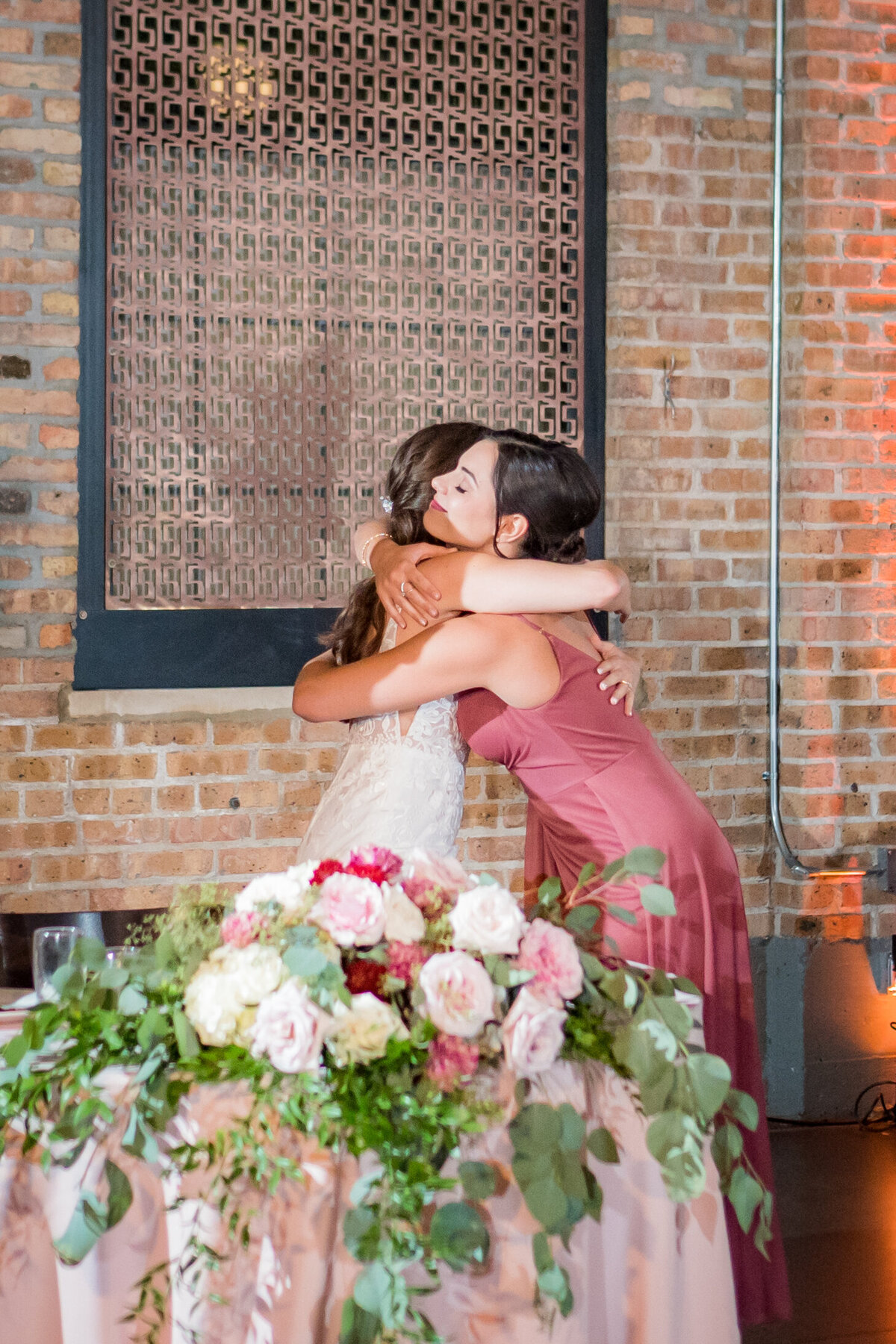Sweetheart table flowers bride hugging bridesmaid