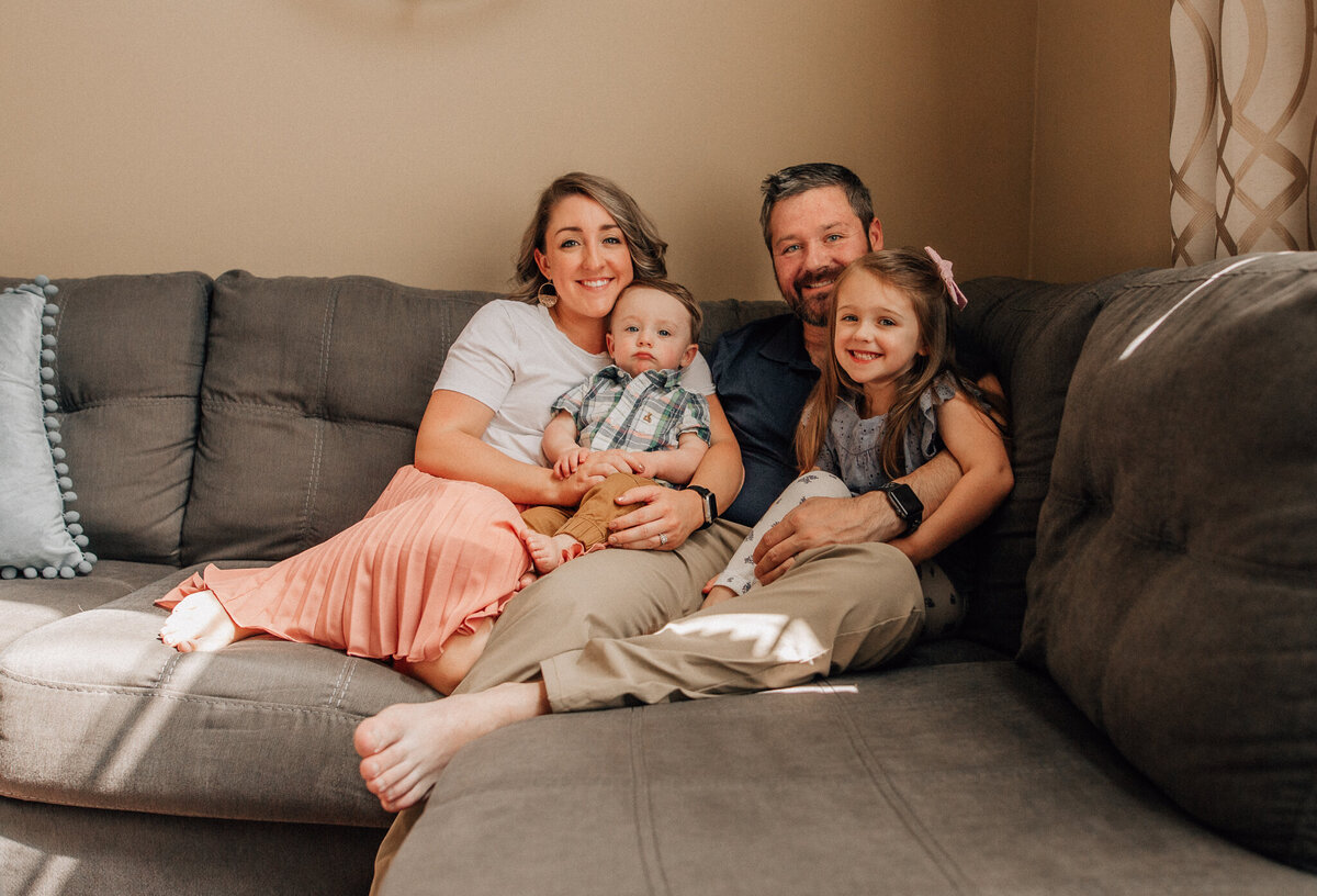 Family photoshoot with mom, dad, and two children sitting on the couch together.