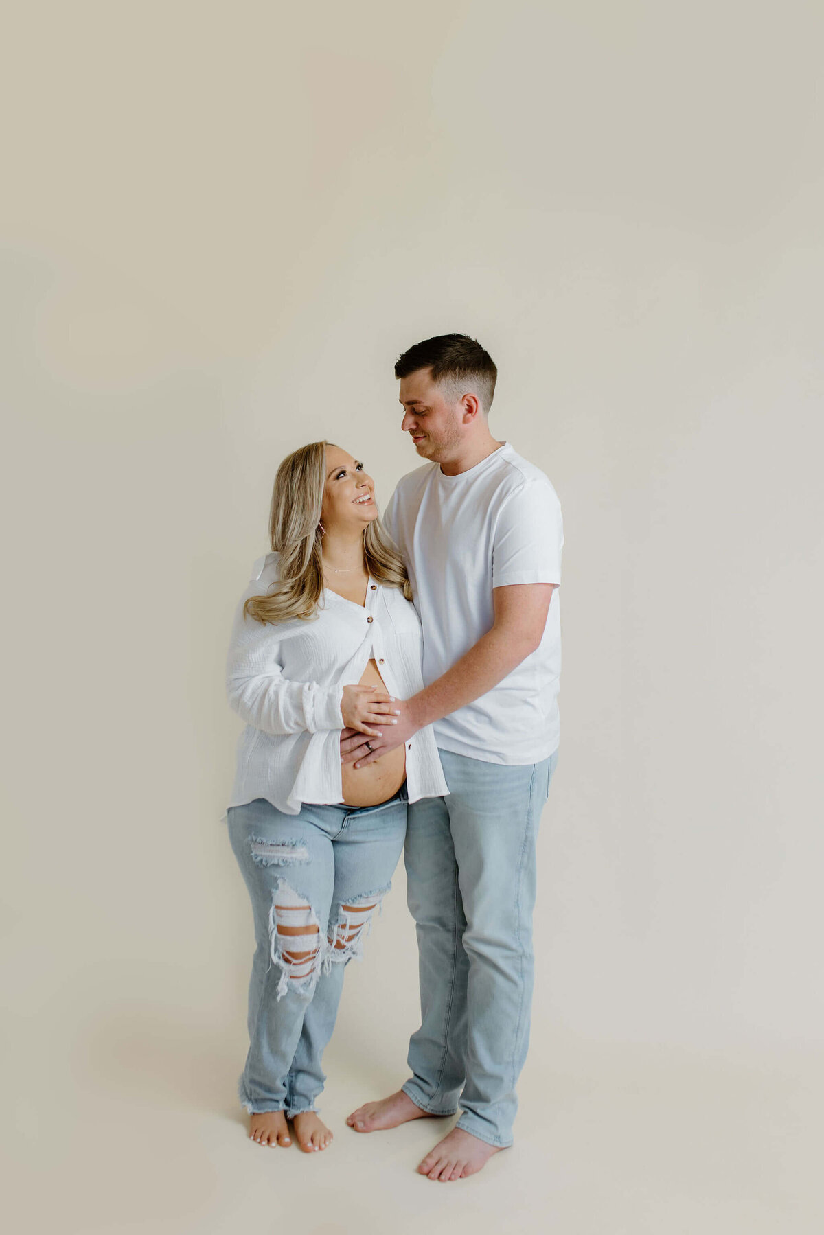 Studio maternity portraits of expecting parents in white shirts and jeans