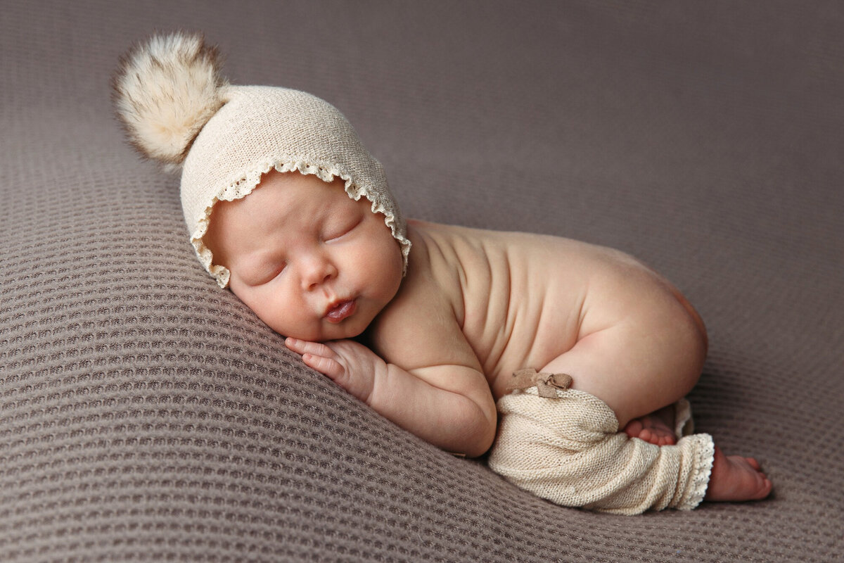 Sleeping Newborn with a cream colored bonnet and leg warmers laying bare botton on her tummy