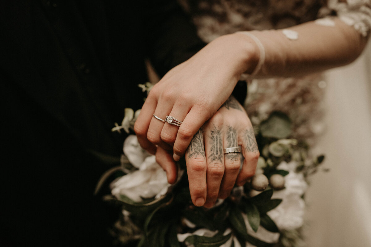 Close up photo of bride and groom holding hands with rings in forest