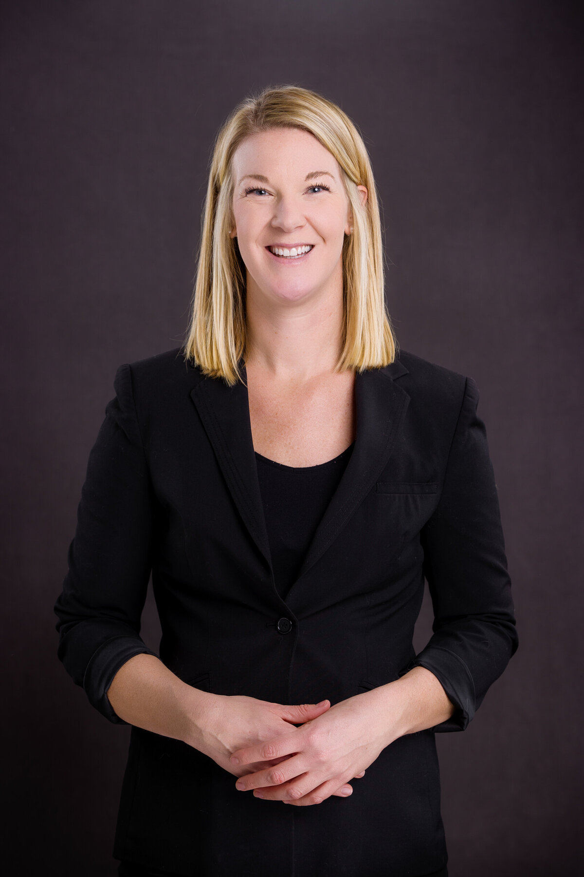 Headshot of a woman wearing a black suit on a grey backdrop