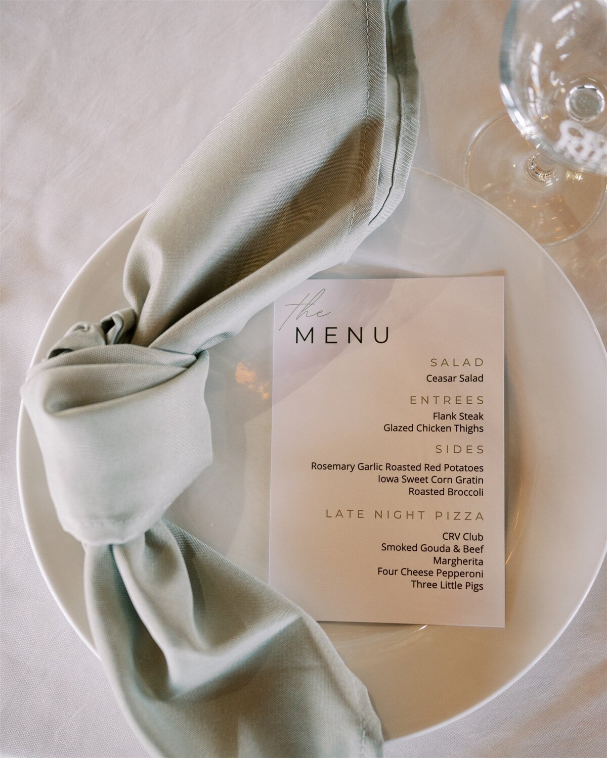 Elegant table setting for a wedding planner Illinois event, featuring a plate with a gray napkin, a menu card listing various dishes, and a clear glass, all arranged on a white tablecloth.