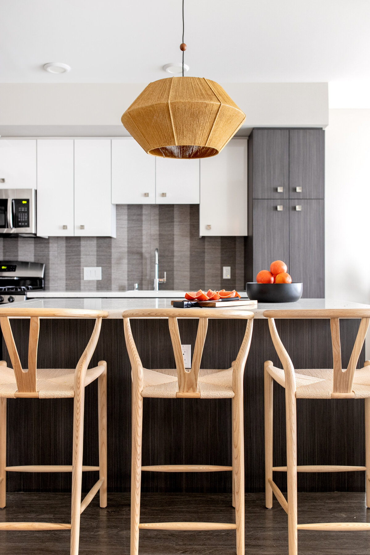 Wishbone natural wood barstools in front of kitchen island with jute pendant hanging above