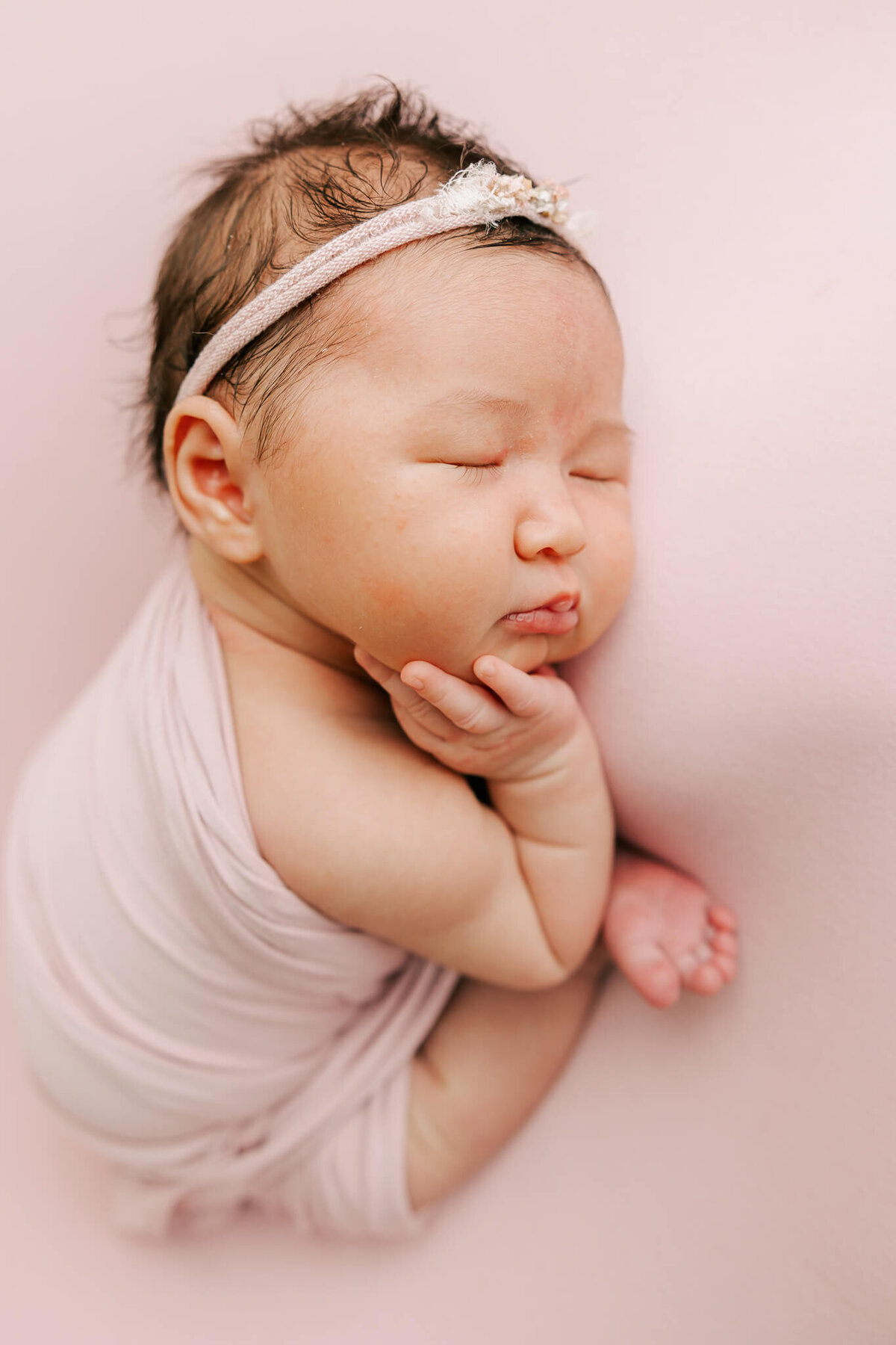 little newborn girl with headband on sleeping on pink blanket