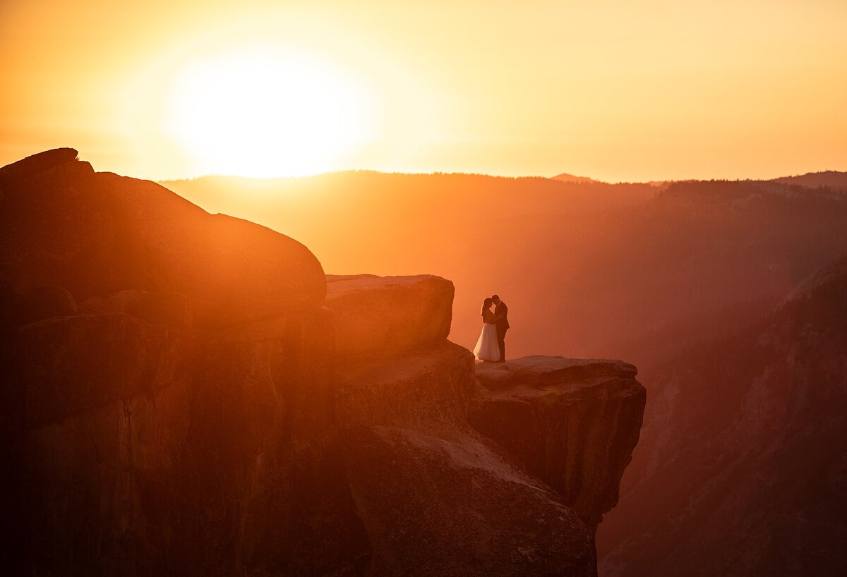 Bride and groom stand on a cliff edge overlooking Yosemite National Park