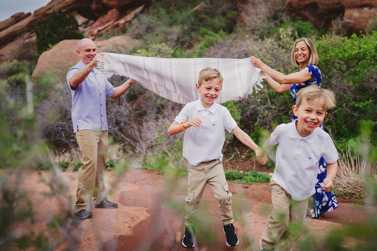 Brothers holding hands and runningunder blanket at Red Rocks Park  in Morrison, Colorado  for their family photos.