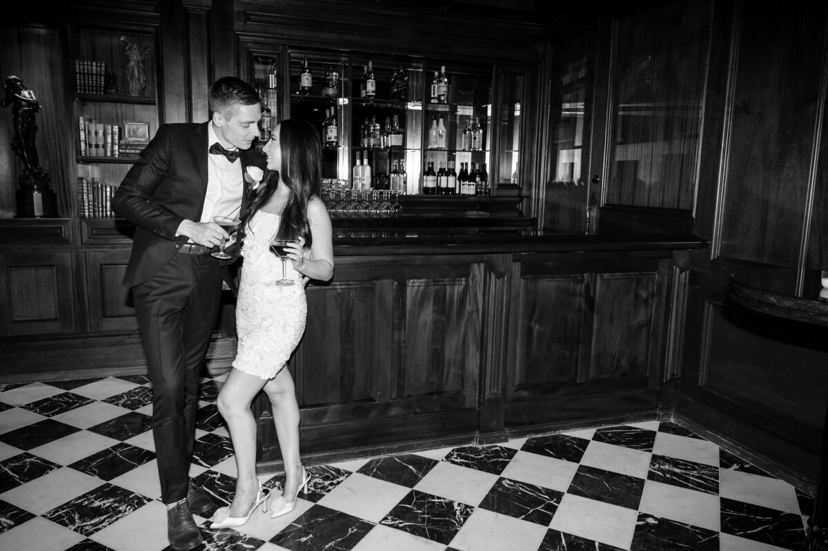 Black and white photo of a couple standing inside the bar at their Park Savoy Wedding.  They are holding martinis.