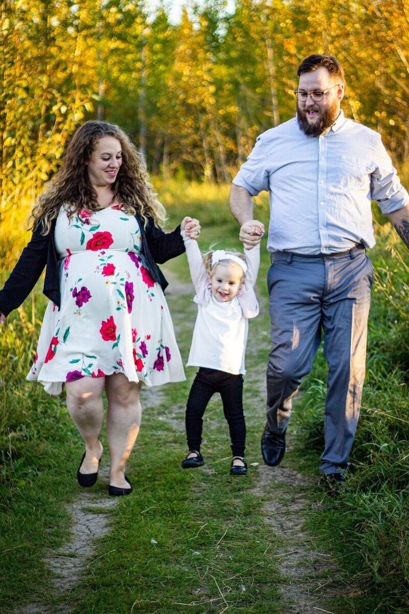 an Edmonton couple swing their daughter in their arms on a dirt road