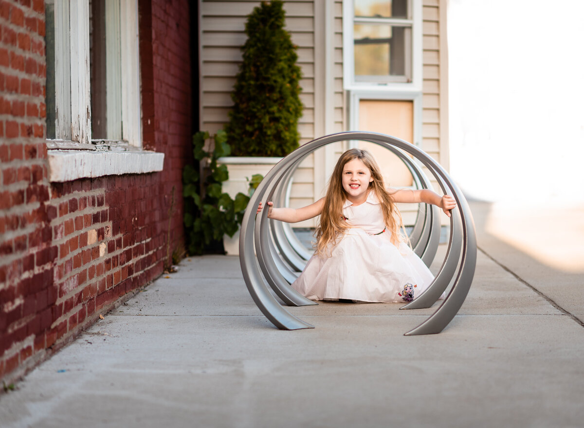 A young girl in a white dress playing in a tunnel of pipes on a city sidewalk