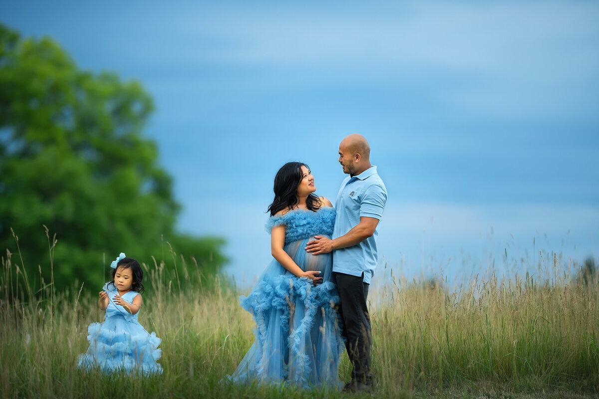 Family pictures of pregnant mother in blue tulle maternity dress with husband and daughter