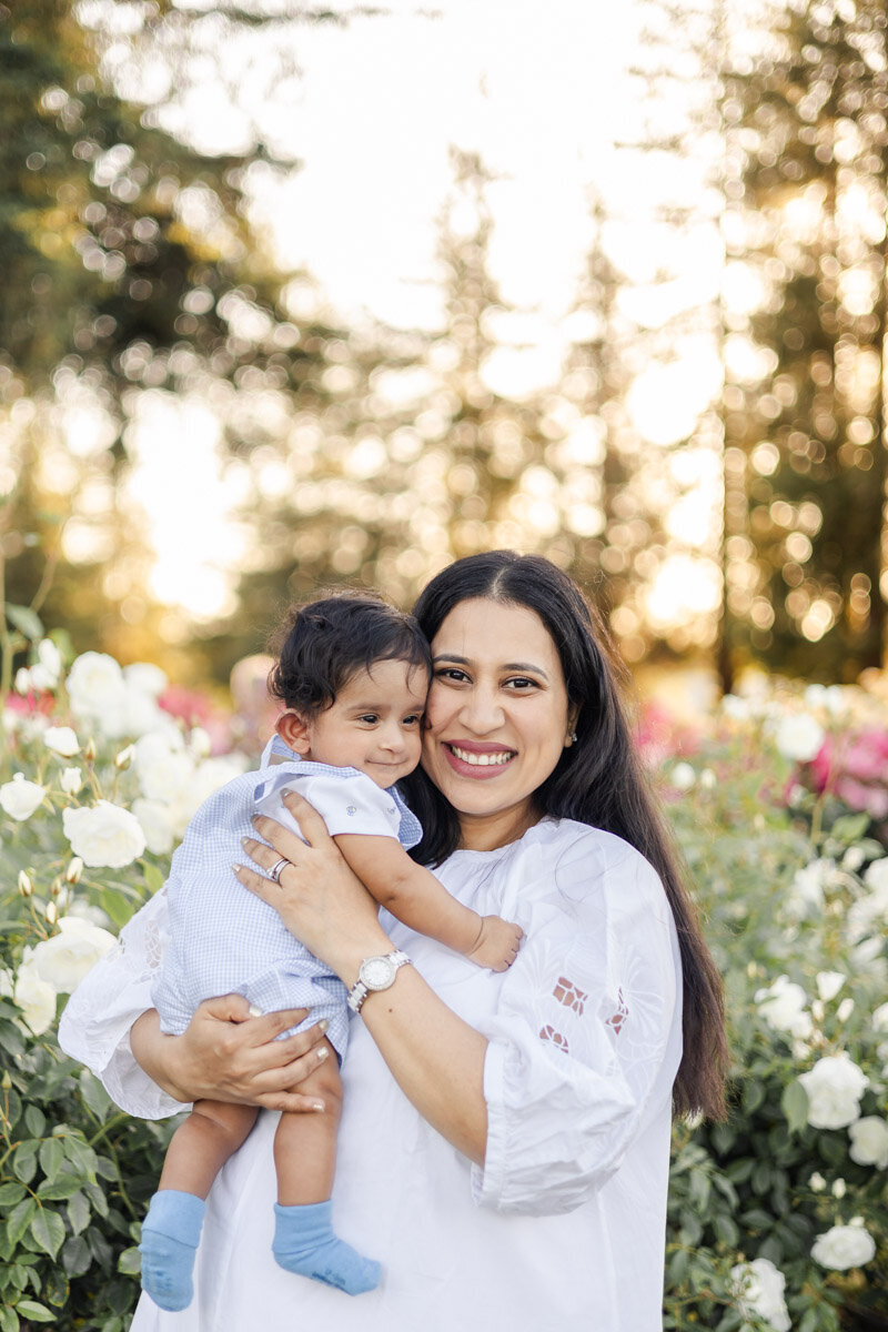 Mom and baby sharing smiles amid blooming roses during golden hour portrait session at San Jose Rose Garden