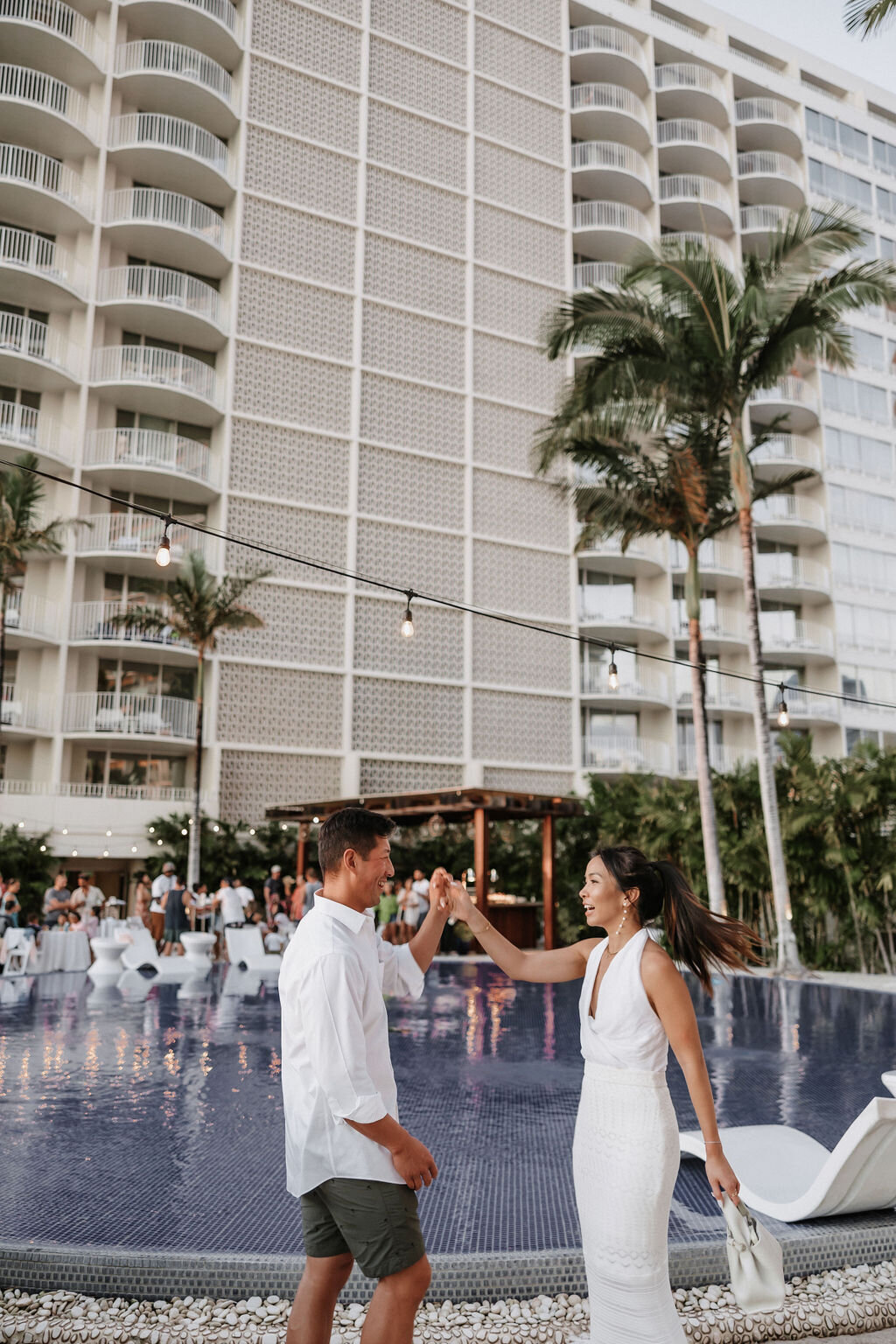 couple dancing in front of pool with guests mingling far behind them