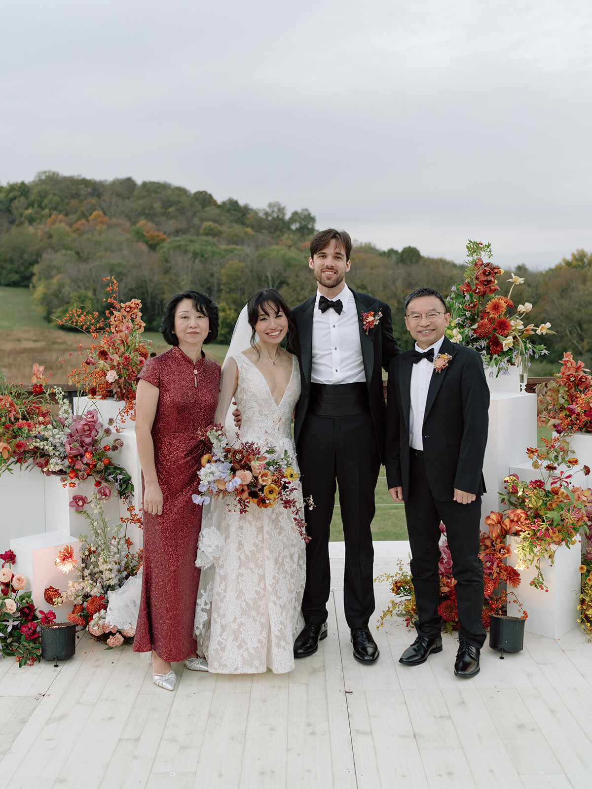 Sculptural columns wedding ceremony backdrop. Stair step white ceremony columns adorned with sculptural floral meadows in fall hues. Clear top tent build out for fall wedding reception in Tennessee hills. Wire threaded orchids, bittersweet berries, butterfly ranunculus, and tulips are highlighted in this wedding ceremony backdrop. Artistic fall color palette in copper, gold, ruby, lavender, and rust. Design by Rosemary & Finch Floral Design in Nashville, TN.