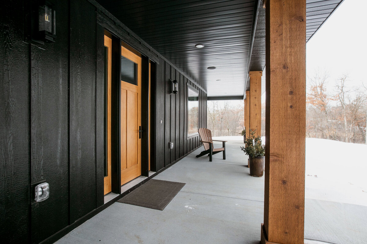 Exterior view of custom home in Elk River, Minnesota with black siding, wood details and front porch built by Cornerstone Custom Builds