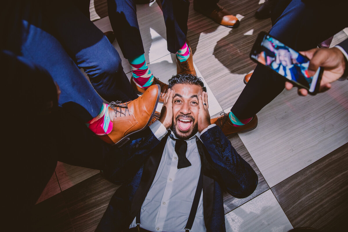 indian christian groom laying on the dance floor showing off his groomsmens' socks