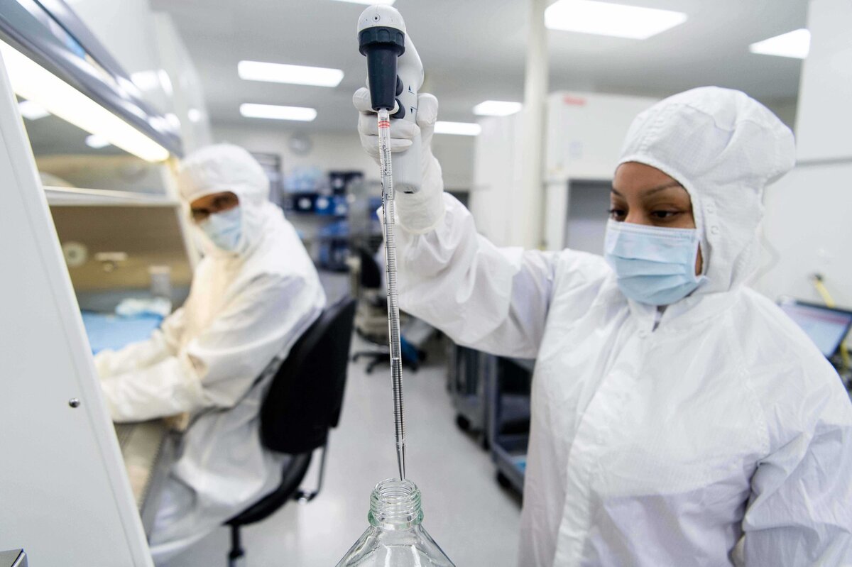 A worker covered in sterile while lab coat and mask uses pipet as another worker looks on. Image shows the production process for medical implants