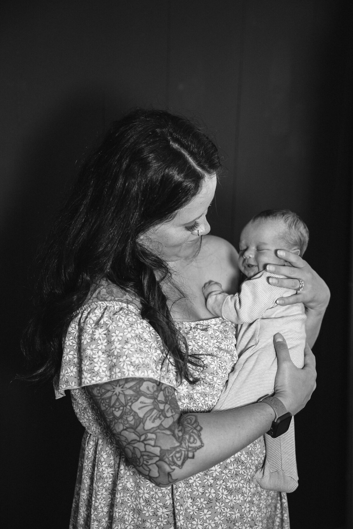 A mother stands in a studio cradling her sleeping newborn against her shoulder