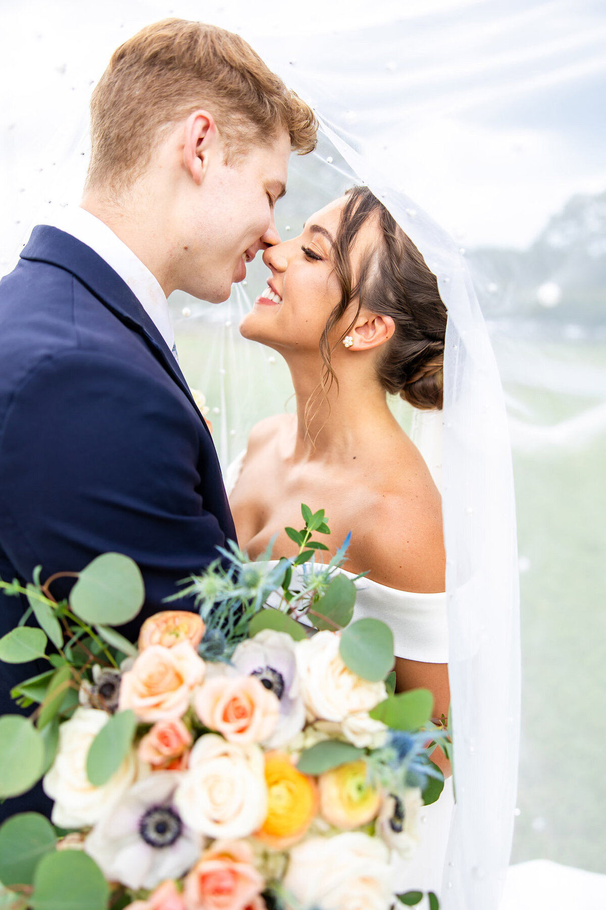 Bride with a bright bouquet gently touching her nose to her husbands nose