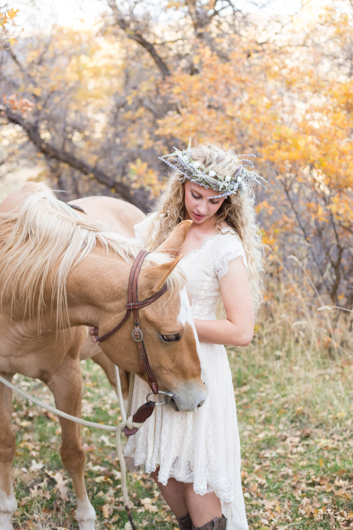 Young woman in a flower crown talking to her palomino horse in the woods