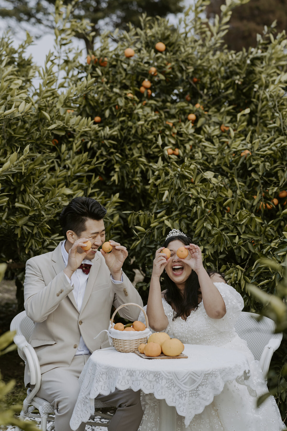 the couple sitting down in a table surrounded by tangerines and they are having fun