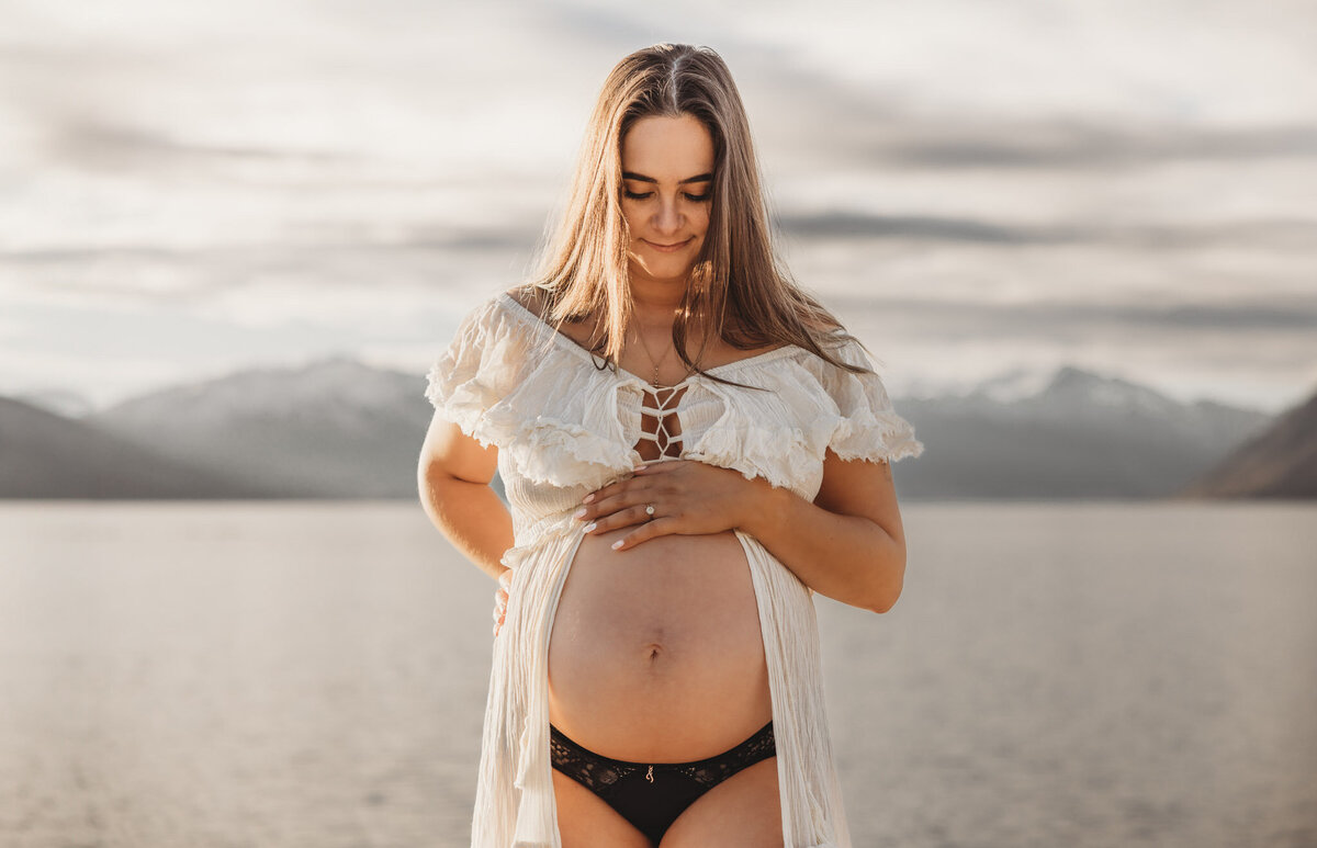 pregnant woman standing with hand on belly in wanaka during her maternity session
