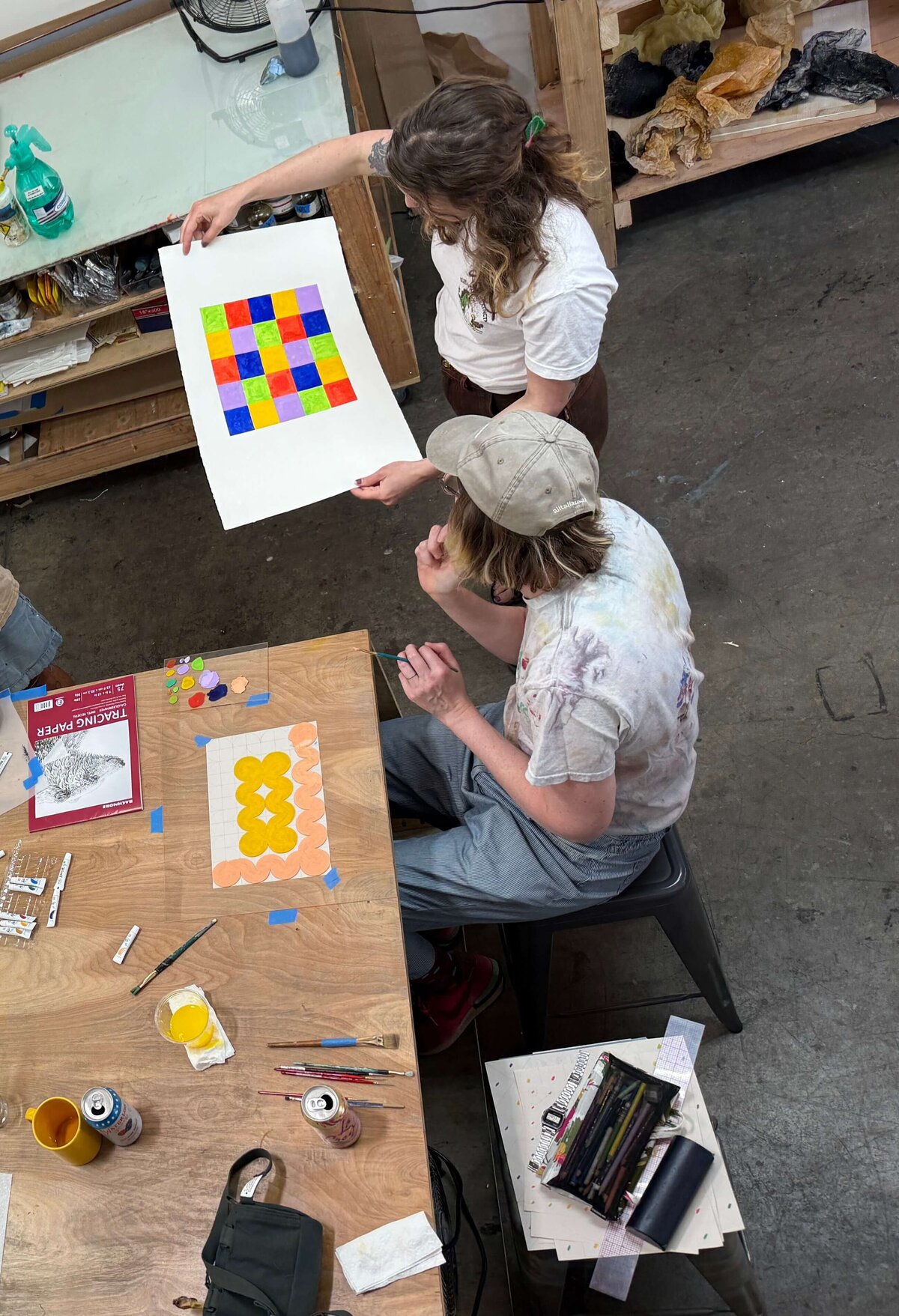 A participant proudly holds up a vibrant multicolored grid print at a monoprinting workshop.