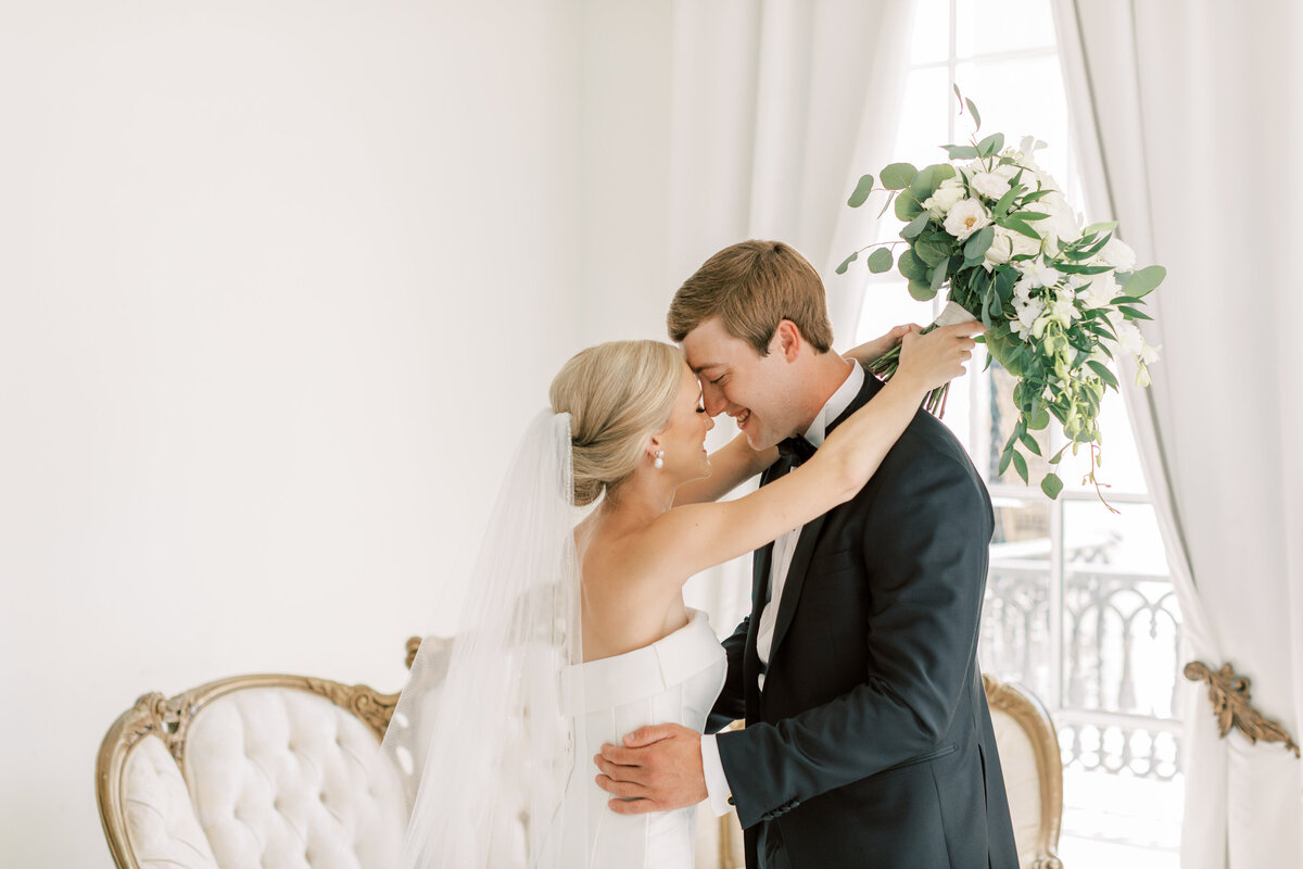 A bride and groom embrace each other in a white room.