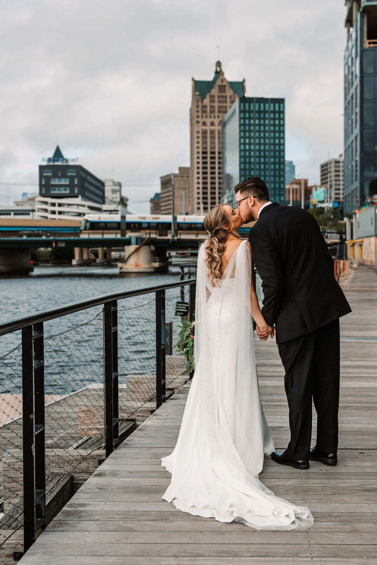 bride and groom kiss while holding hands with their backs to the camera on the milwuakee riverfront