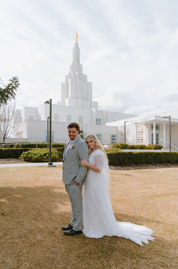 A closer version of the bride holding the arm of her fiancé as she looks at the camera and smiles. He is facing the same way as she is.