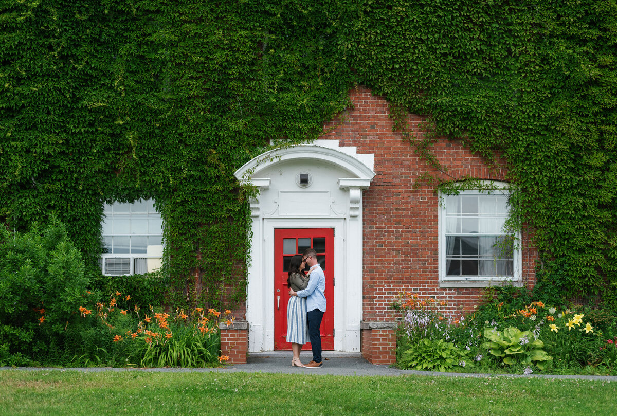 Couple standing in front of red door with red brick building covered in vines.