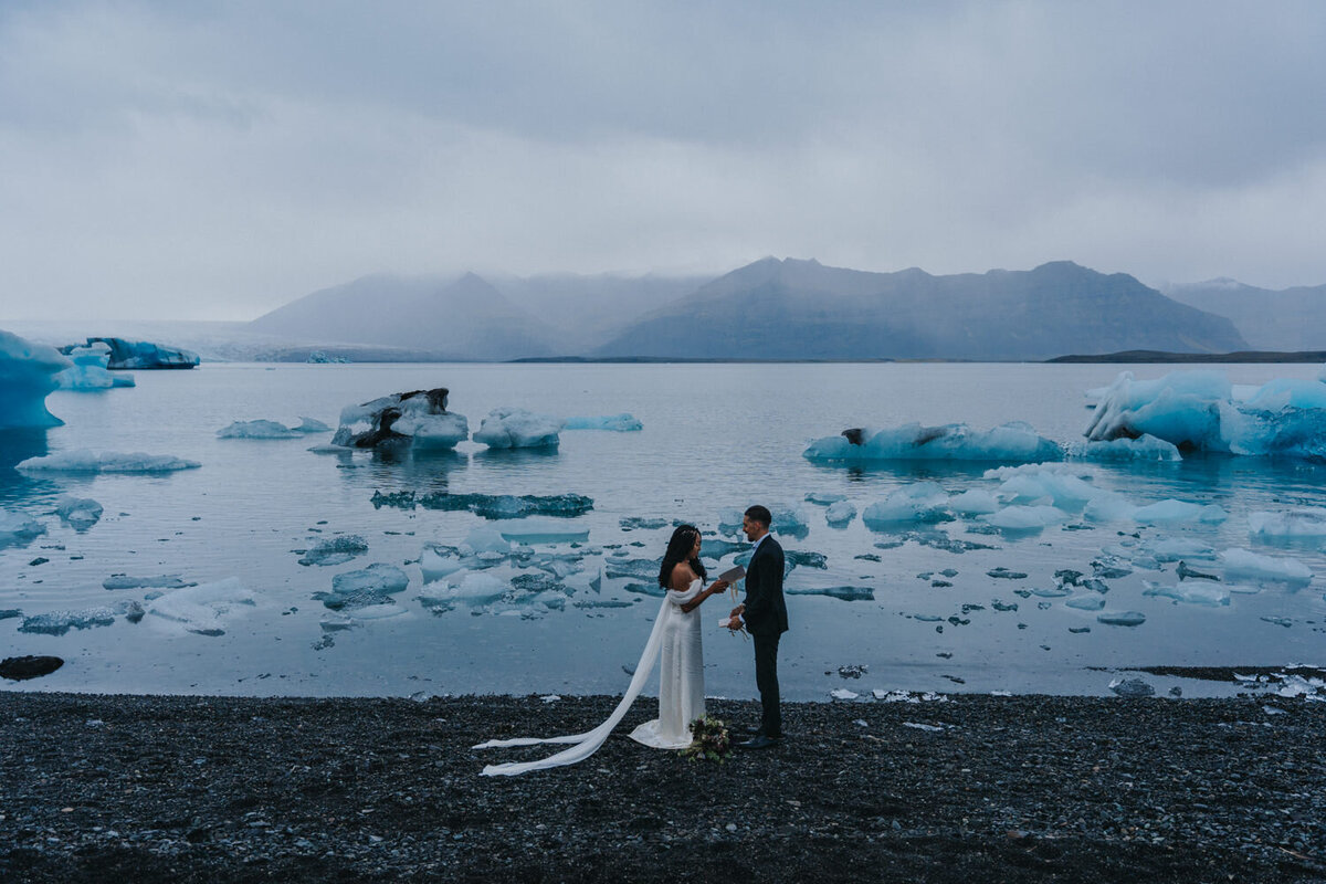 Wife reads vows from her notebook while standing on the shore of the Iceland Black Sand Beach