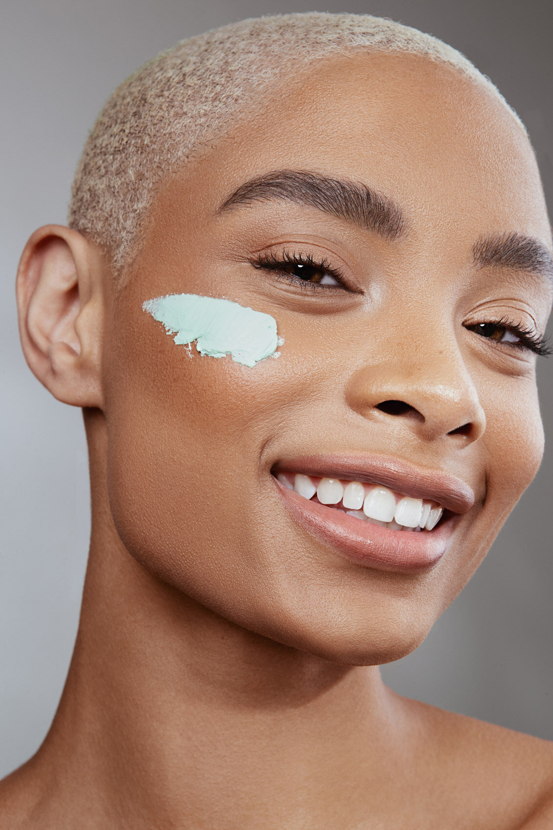 Smiling beauty portrait of Raven with under-eye cream applied, showcasing glowing skin, captured by Ylva Erevall.