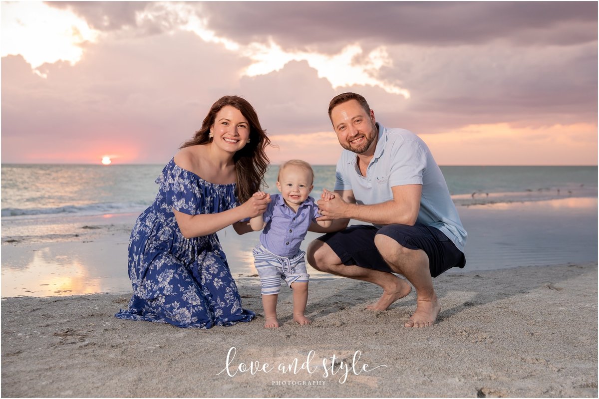 young parents with their toddler smiling for their Anna Maria Island family photographer at sunset