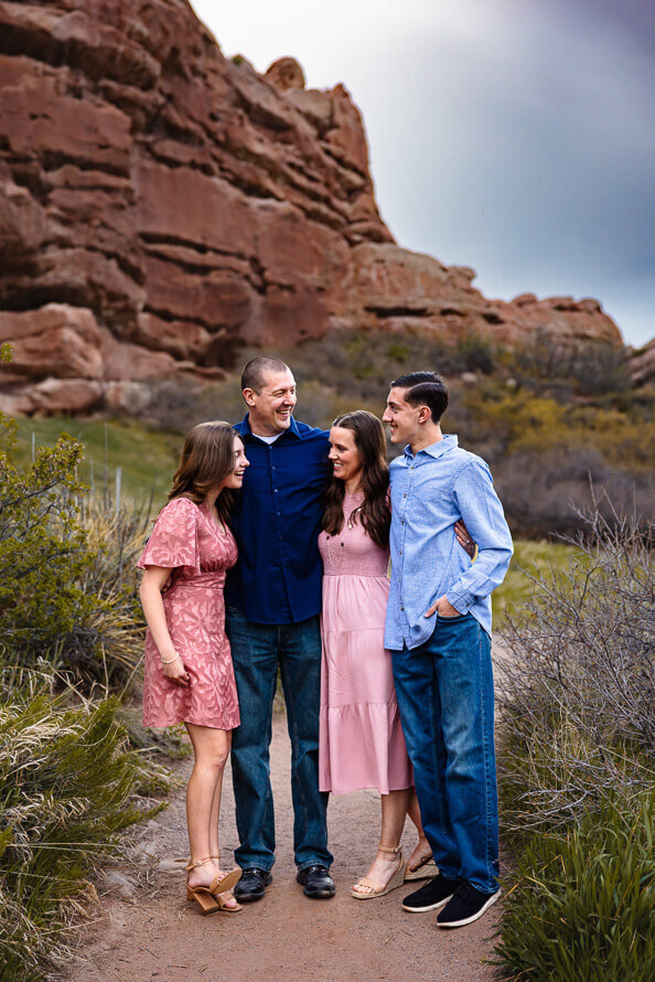 A family of four look at each other in front of red rock formations.