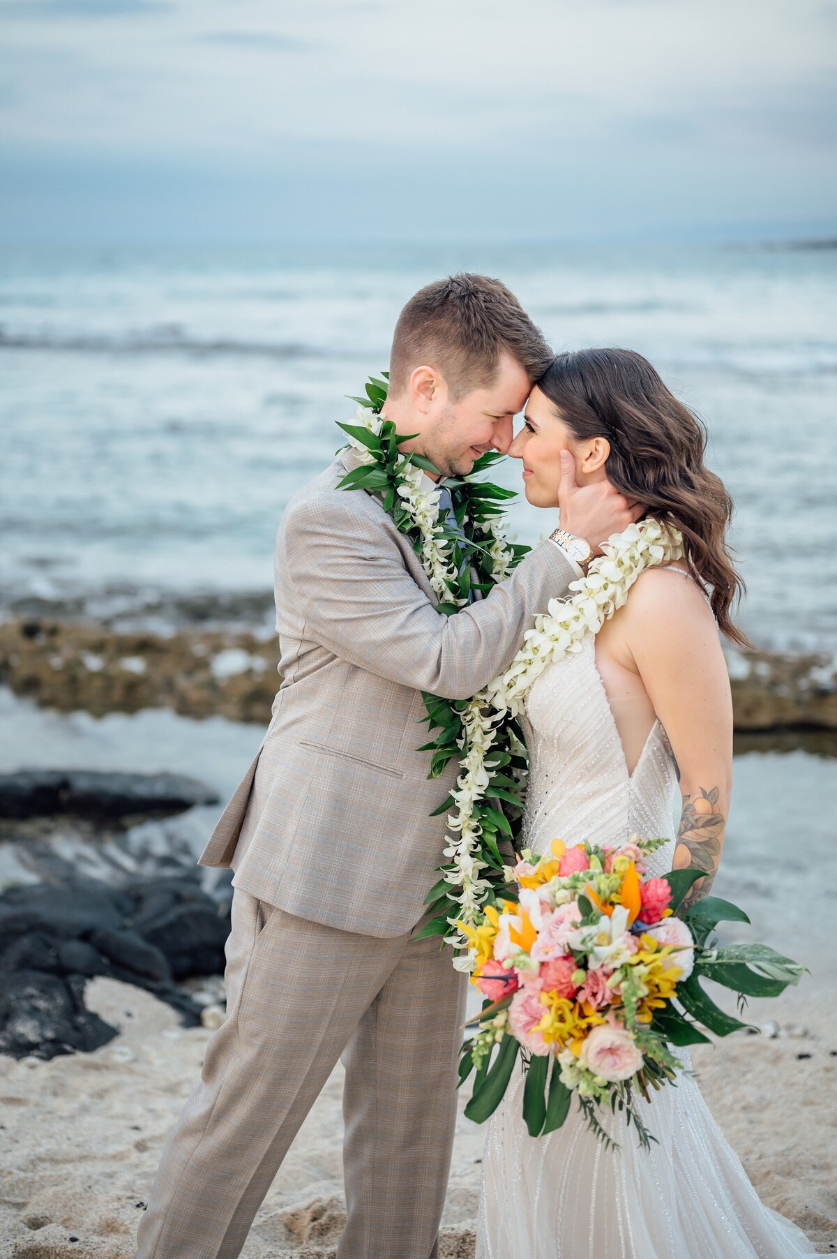 groom holds bride close after their elopement ceremony on the beach