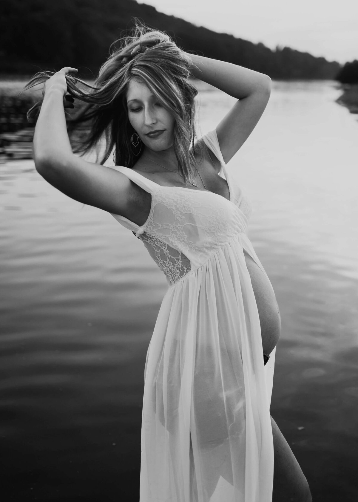 A pregnant woman in a white dress posed by the water, captured beautifully by a Pittsburgh maternity photographer.