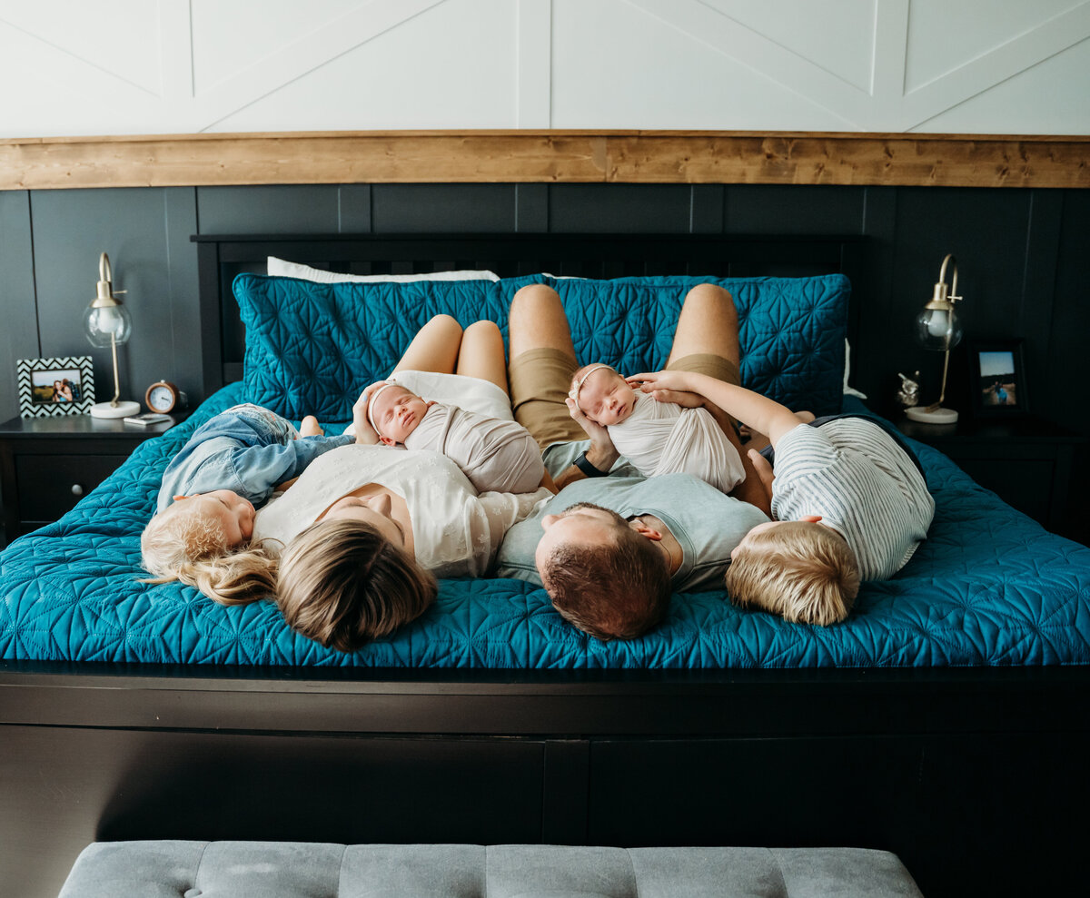 Newborn Photographer, mom, dad and two brothers lay on the bed with twin babies on parents lap