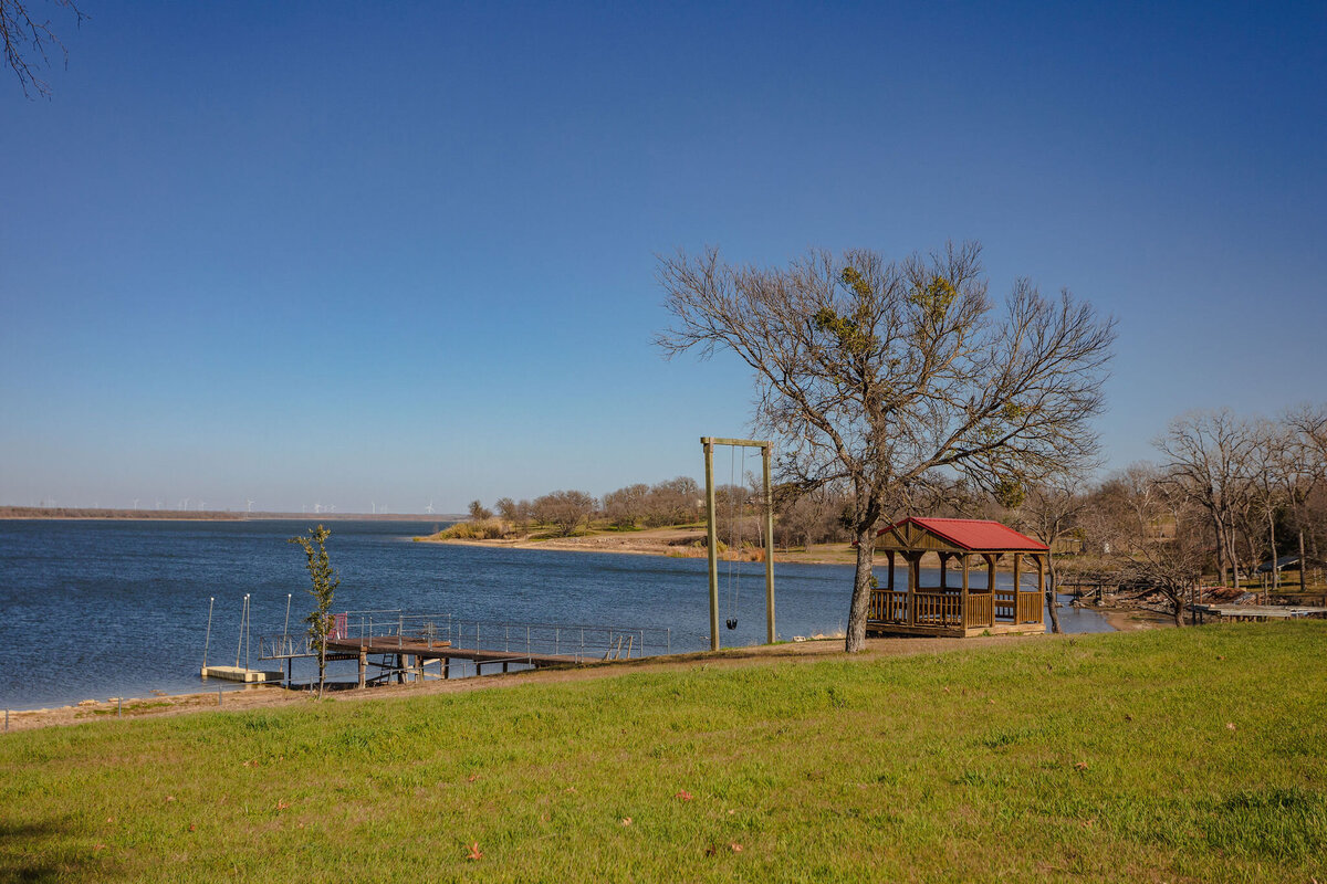 Spacious backyard area with swing, covered patio and dock access at this 2-bedroom, 2-bathroom lakeside vacation rental home for 6 guests on Tradinghouse Lake with privacy access to a fishing dock and boat launch pad, ping pong table, gazebo, free wifi and free parking in Waco, TX.