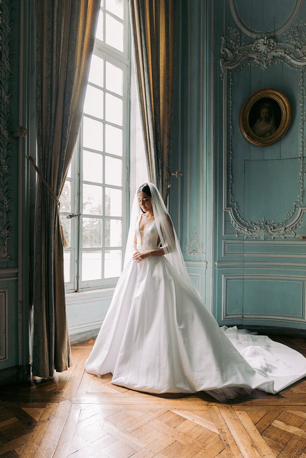 Bride standing next to a window in a room in Chateau de Champlatreux