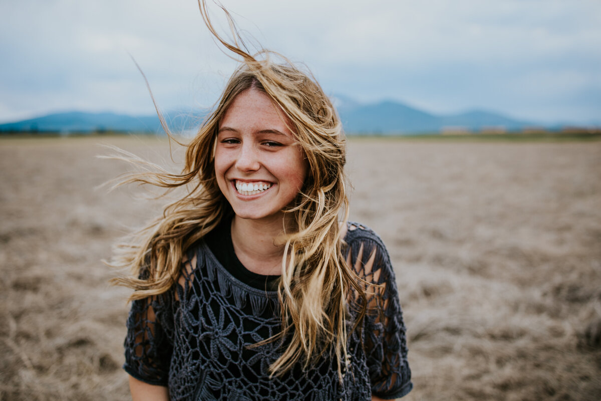 Singer smiles standing in a field while wind blows her hair around.