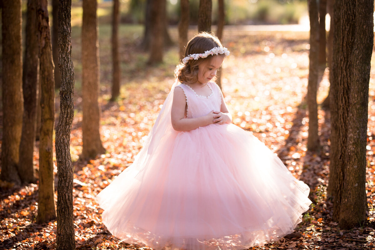 Girl-In-pink-dress-and-white-floral-crown-looking-down-in-the-forest-of-trees
