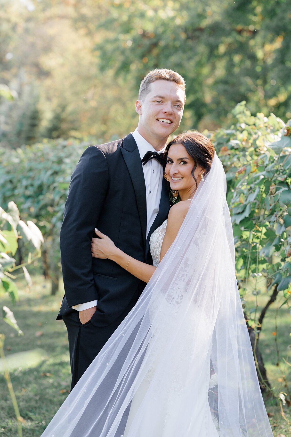 wedding photo at a vineyard with bride holding his groom around his torso and he leans into her and smiles captured by Columbus wedding  photographer