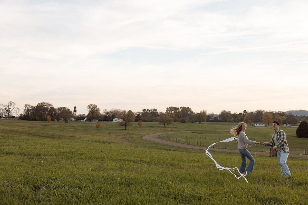 Couple joyfully runs through the rolling hills of Franklin, TN while flying a kite. 