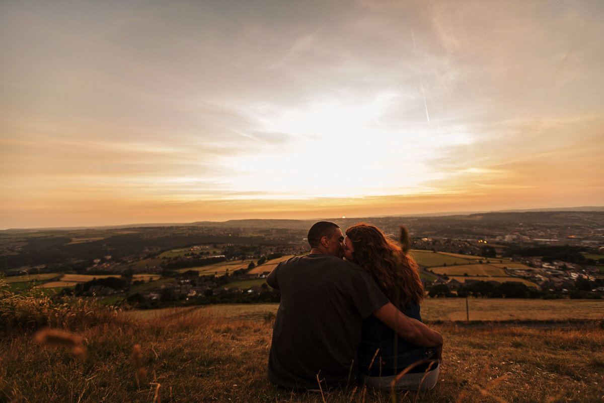 An engagement shoot photograph of a couple sat on the Yorkshire Moors as the sun sets