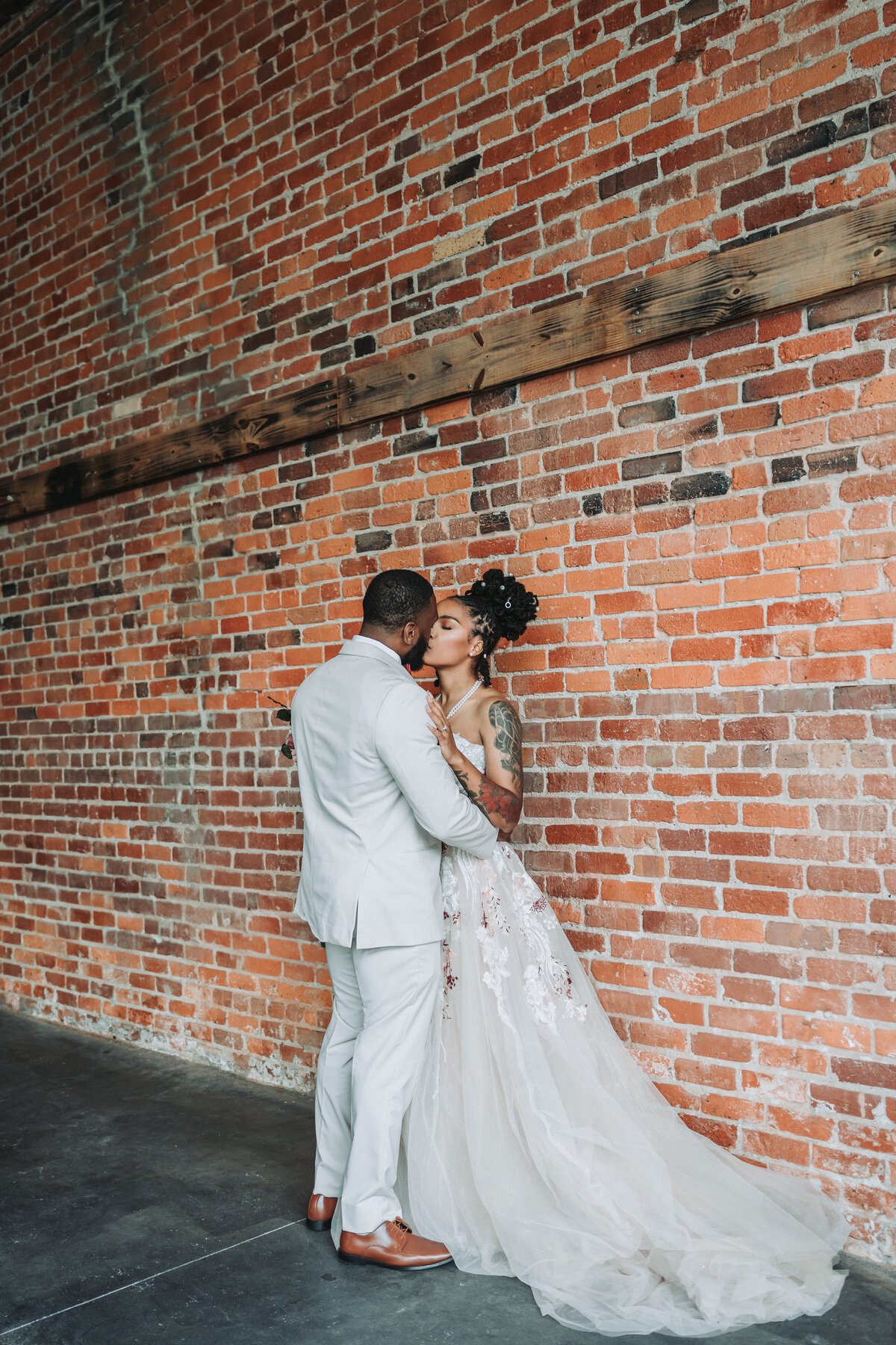 Bride and groom embrace in front of a rustic brick wall at The Neon House wedding venue in Norfolk, Virginia.