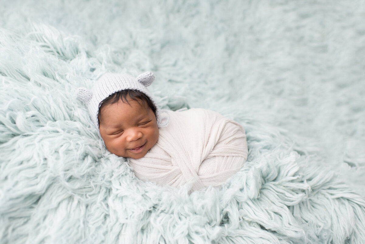 a newborn wrapped in a blanket on top of a baby blue fur backdrop