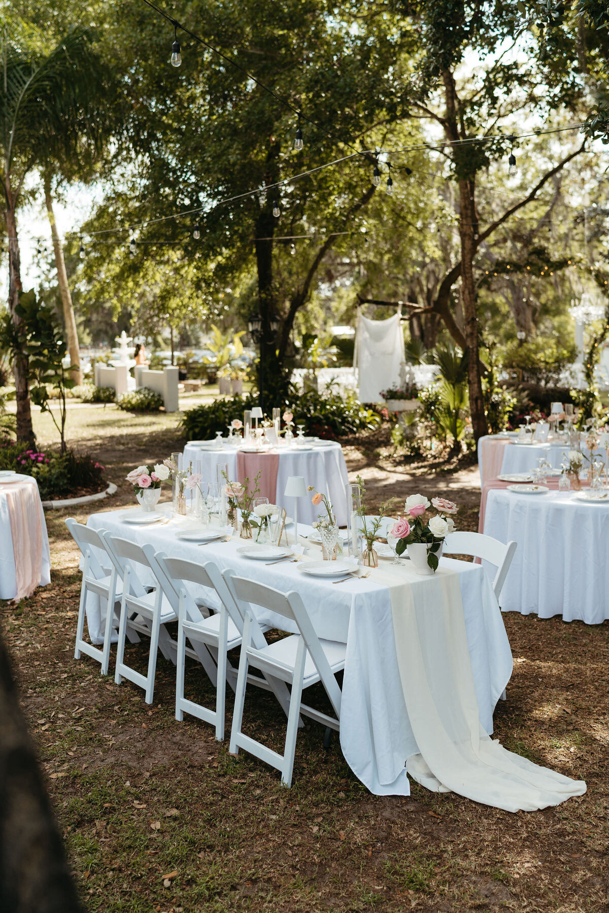 Outdoor reception setup with white tables beneath the trees at Uliana Estate in Lakeland Florida.