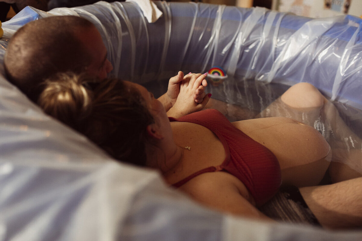 Tifton, GA birth photography: soon-to-be Mom leaning back against her partner in birthing tub, holding hands
