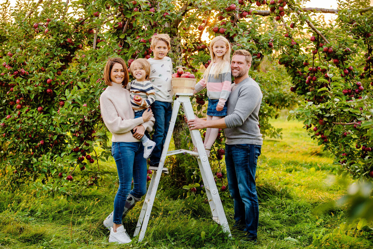 Family of five standing on a white ladder in an apple orchard for their fall family photos in Burlington, ON